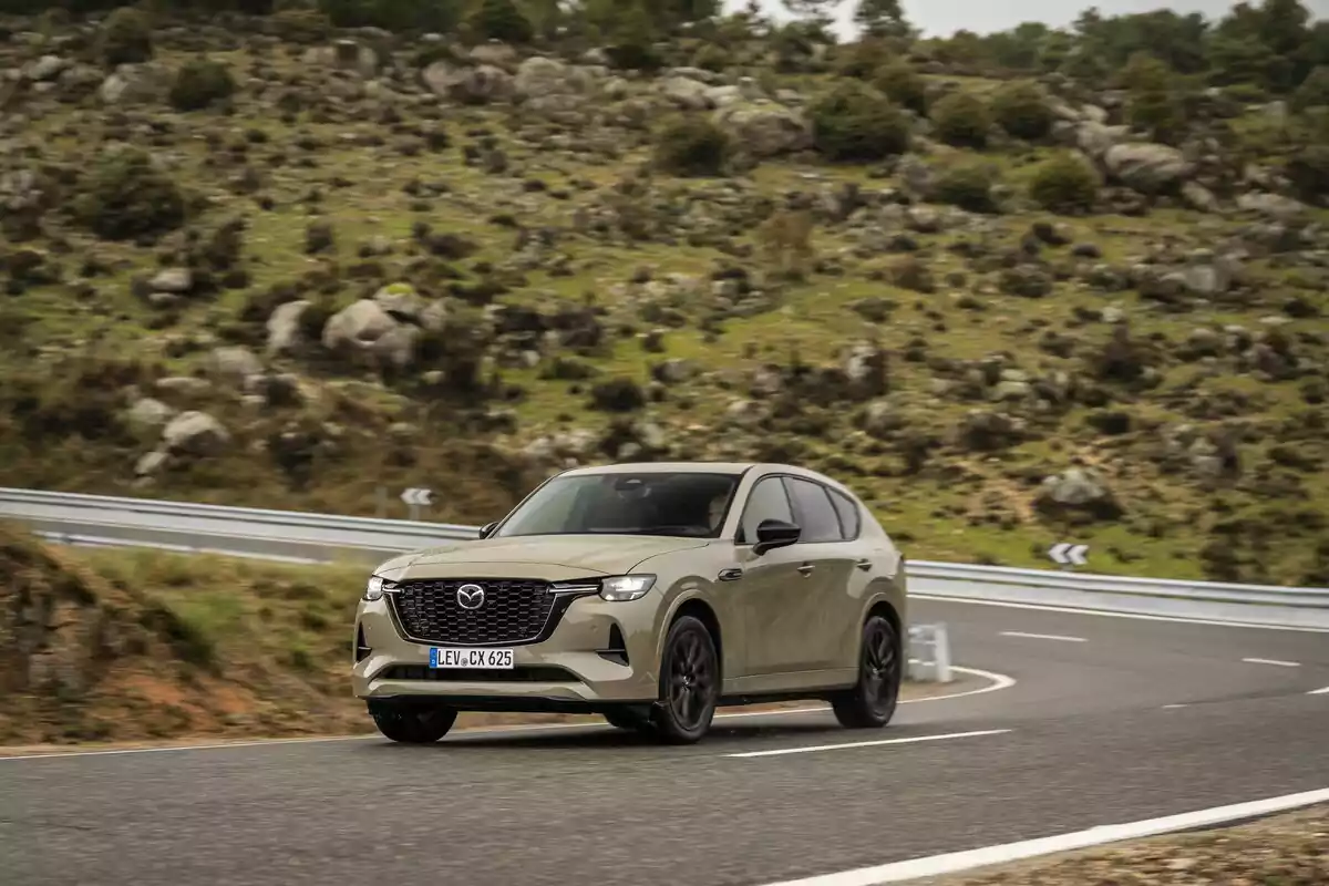SUV beige de Mazda conduciendo por una carretera de montaña con curvas y vegetación alrededor