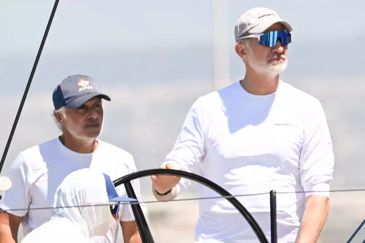 Tres hombres con camisetas blancas y gorras navegan en un velero bajo el sol Tres hombres con camisetas blancas y gorras navegan en un velero bajo el sol