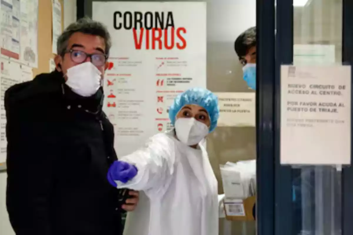 Personal médico con mascarilla y bata protectora señala una dirección mientras acompaña a un hombre con cubrebocas en un centro de salud durante la pandemia de coronavirus Personal médico con mascarilla y bata protectora señala una dirección mientras acompaña a un hombre con cubrebocas en un centro de salud durante la pandemia de coronavirus