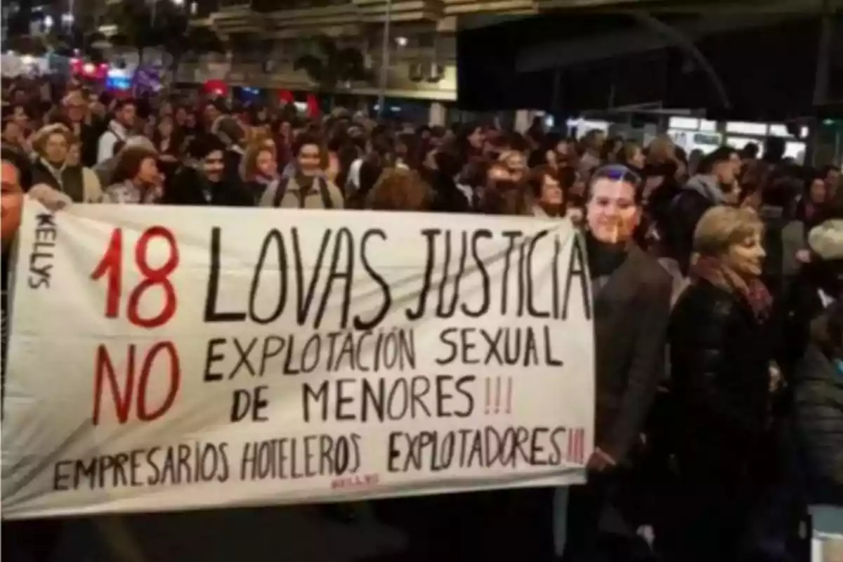 Manifestación nocturna con un grupo de personas sosteniendo una pancarta que exige justicia y denuncia la explotación sexual de menores y la explotación laboral en el sector hotelero Manifestación nocturna con un grupo de personas sosteniendo una pancarta que exige justicia y denuncia la explotación sexual de menores y la explotación laboral en el sector hotelero