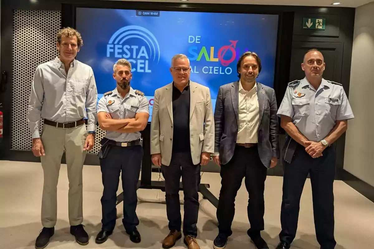 Cinco hombres posan frente a una pantalla que muestra el logo de un evento llamado Festa del Cel de Salou al Cielo, dos de ellos llevan uniforme y los otros tres visten ropa formal.