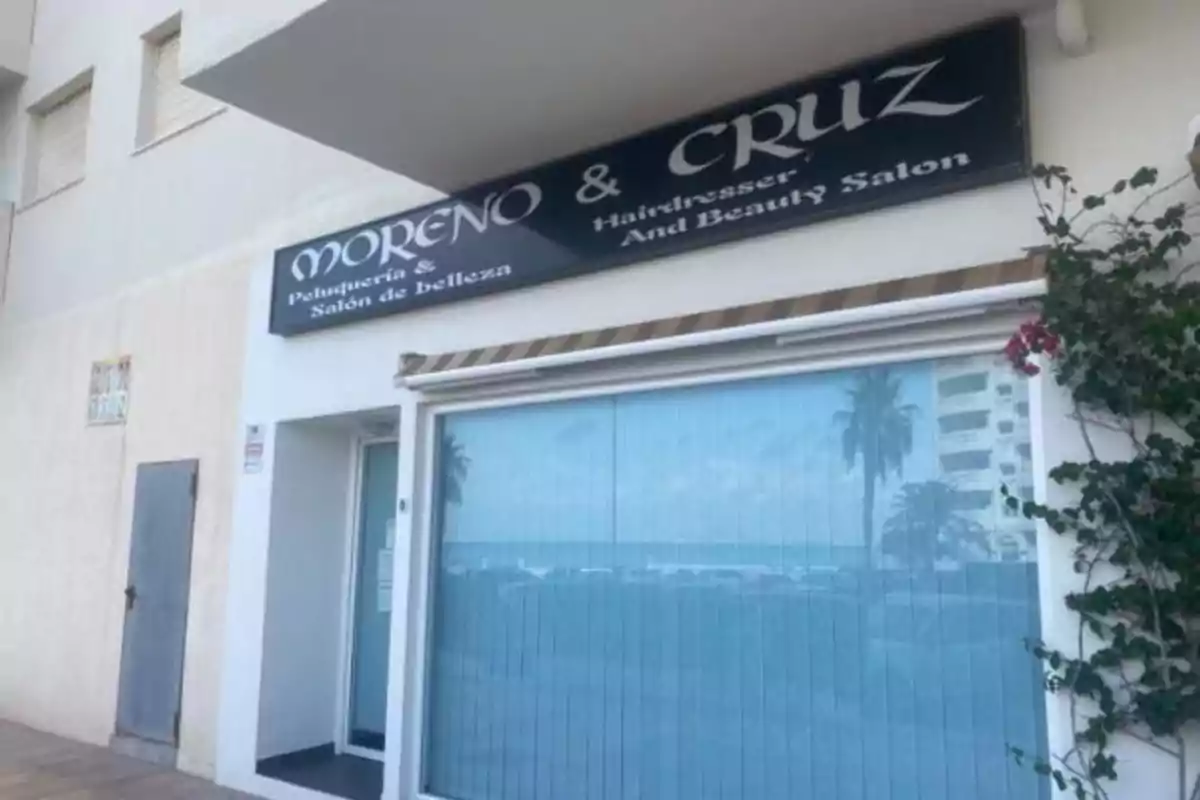 Fachada de una peluquería y salón de belleza llamada Moreno & Cruz con un letrero en español e inglés y una ventana grande con persianas azules