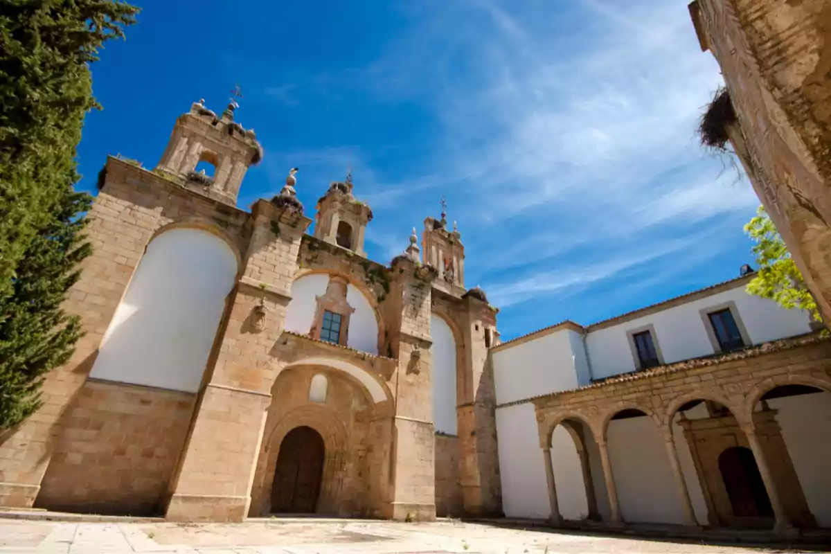 Fachada de un antiguo monasterio de piedra con arcos y campanarios bajo un cielo azul despejado Fachada de un antiguo monasterio de piedra con arcos y campanarios bajo un cielo azul despejado