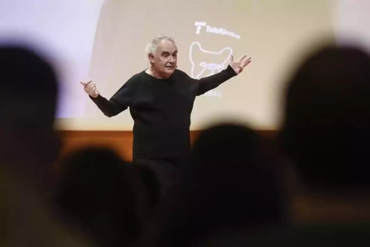 Hombre de cabello canoso y suéter negro dando una conferencia frente a una audiencia con una pantalla de fondo. Hombre de cabello canoso y suéter negro dando una conferencia frente a una audiencia con una pantalla de fondo.