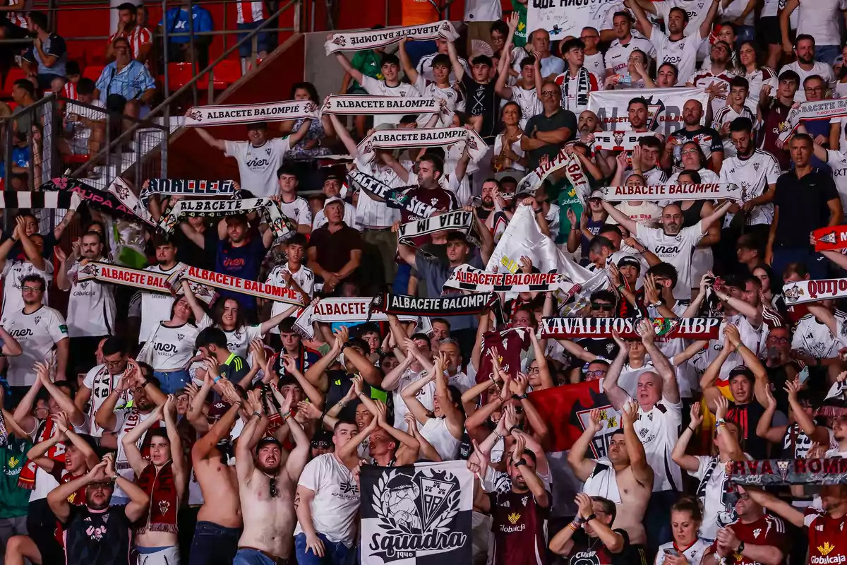 Aficionados del Albacete Balompié animando en las gradas con bufandas y camisetas del equipo, mostrando entusiasmo y apoyo durante un partido de fútbol. Aficionados del Albacete Balompié animando en las gradas con bufandas y camisetas del equipo, mostrando entusiasmo y apoyo durante un partido de fútbol.