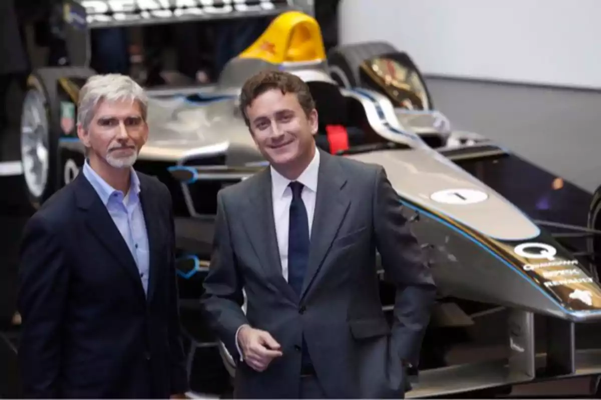 Dos hombres con traje posan frente a un auto de carreras de Fórmula E en un evento de presentación. Dos hombres con traje posan frente a un auto de carreras de Fórmula E en un evento de presentación.