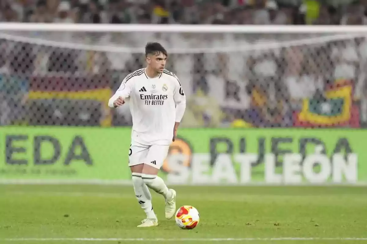 Futbolista del Real Madrid controlando el balón en un partido con la portería y aficionados de fondo Futbolista del Real Madrid controlando el balón en un partido con la portería y aficionados de fondo