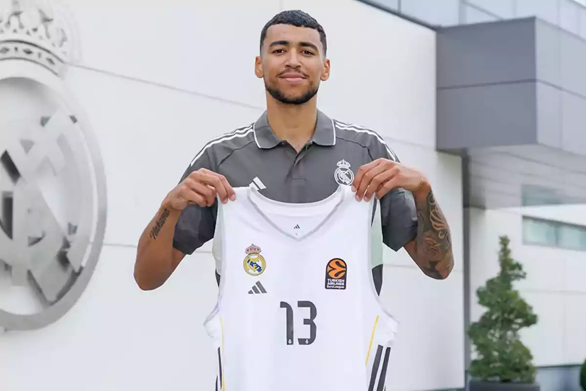 Jugador de baloncesto sosteniendo una camiseta blanca del Real Madrid con el número 13 frente a las instalaciones del club