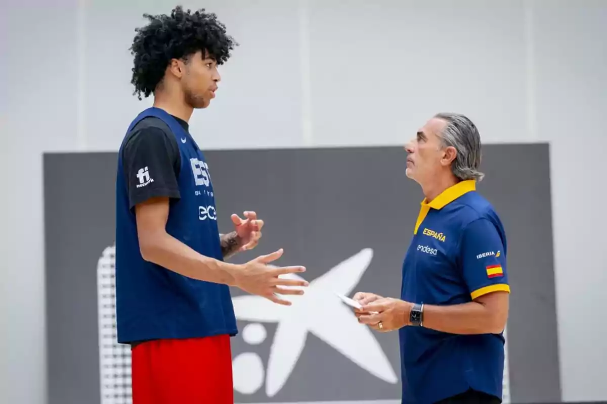 Un jugador de baloncesto y un entrenador conversan en una cancha durante un entrenamiento del equipo de España. Un jugador de baloncesto y un entrenador conversan en una cancha durante un entrenamiento del equipo de España.