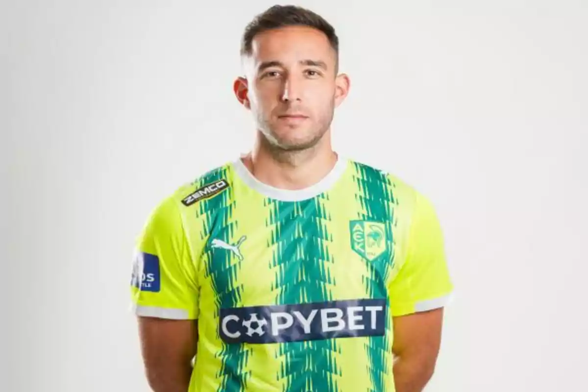 Jugador de fútbol con camiseta amarilla y verde del equipo AEK Larnaca posando frente a un fondo claro Jugador de fútbol con camiseta amarilla y verde del equipo AEK Larnaca posando frente a un fondo claro