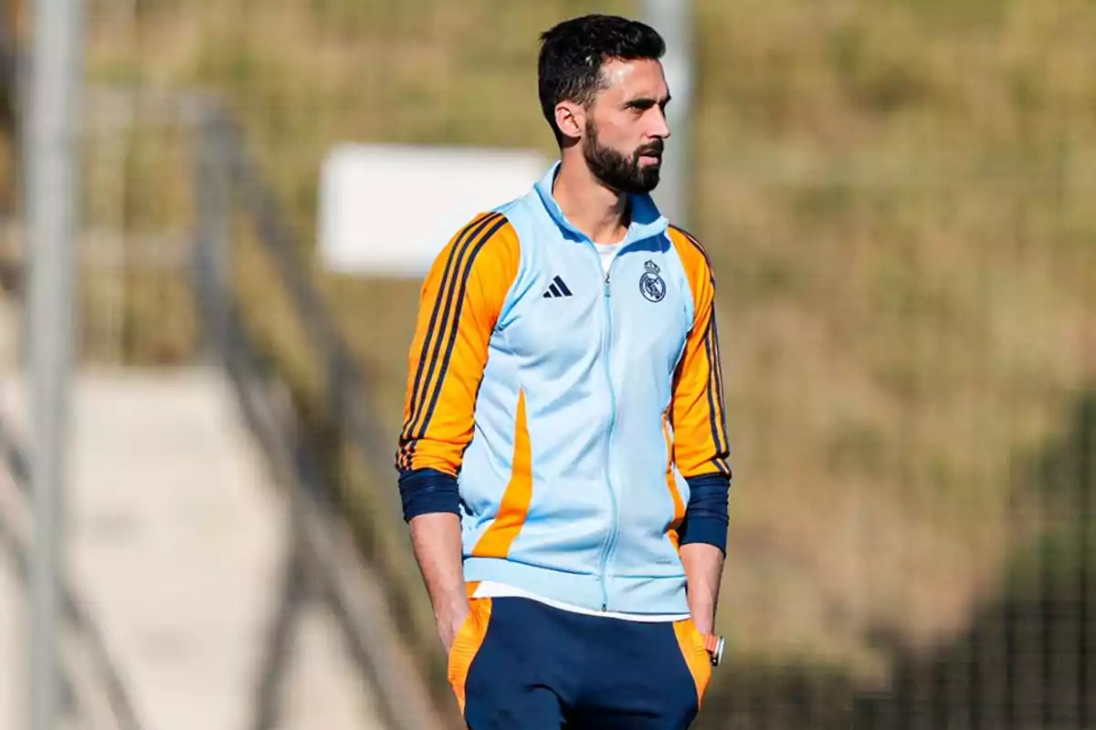 Hombre con barba usando un chándal azul claro y naranja del Real Madrid de pie al aire libre Hombre con barba usando un chándal azul claro y naranja del Real Madrid de pie al aire libre