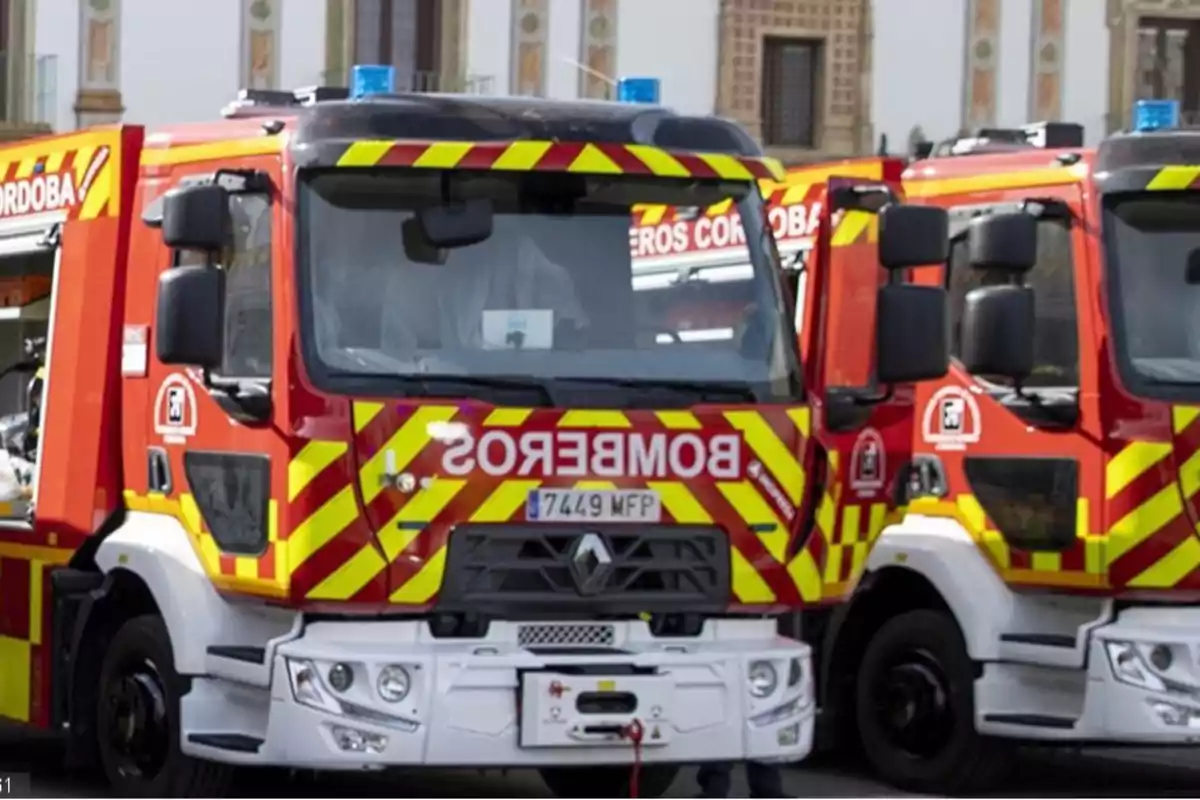 Camiones de bomberos rojos con franjas amarillas estacionados frente a un edificio antiguo Camiones de bomberos rojos con franjas amarillas estacionados frente a un edificio antiguo