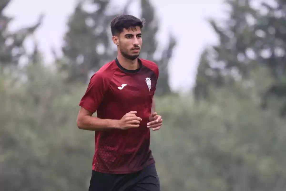 Joven con camiseta deportiva roja corriendo al aire libre con árboles de fondo desenfocado Joven con camiseta deportiva roja corriendo al aire libre con árboles de fondo desenfocado