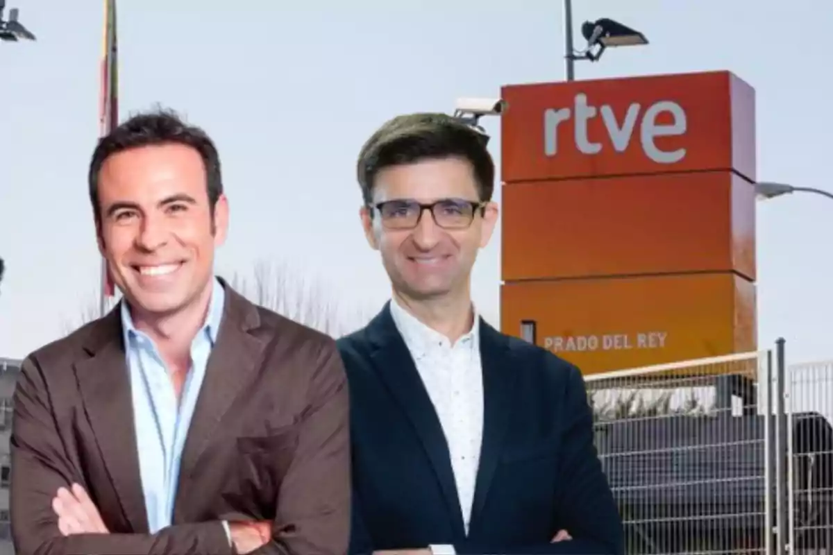 Dos hombres sonrientes posan frente a un letrero de RTVE en el exterior de un edificio