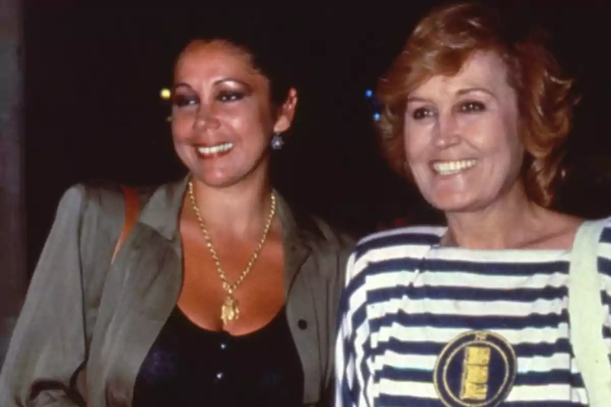 Dos mujeres sonríen mientras posan juntas en una fotografía tomada en un ambiente nocturno Dos mujeres sonríen mientras posan juntas en una fotografía tomada en un ambiente nocturno
