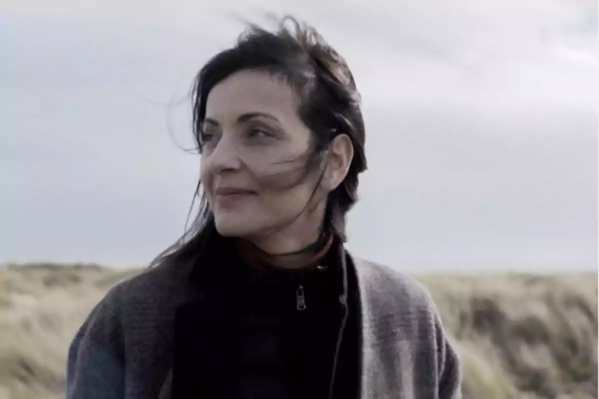 Mujer de cabello oscuro mirando hacia la izquierda en un paisaje al aire libre con viento y cielo nublado Mujer de cabello oscuro mirando hacia la izquierda en un paisaje al aire libre con viento y cielo nublado
