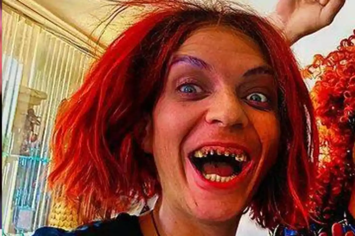 Persona con cabello rojo y corto sonriendo ampliamente mostrando los dientes en un ambiente interior iluminado Persona con cabello rojo y corto sonriendo ampliamente mostrando los dientes en un ambiente interior iluminado
