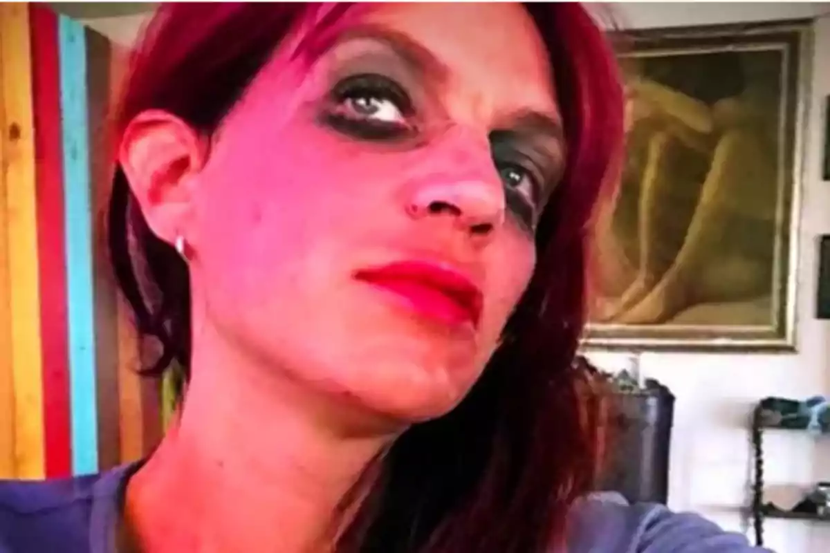 Persona con maquillaje oscuro en los ojos y labios rojos mirando hacia arriba en un ambiente interior colorido Persona con maquillaje oscuro en los ojos y labios rojos mirando hacia arriba en un ambiente interior colorido