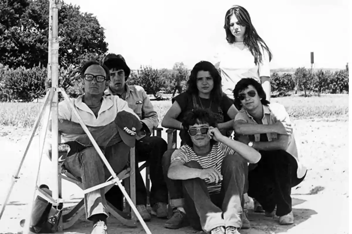 Grupo de seis personas posando al aire libre en un día soleado, algunos sentados y otros de pie, con árboles y vegetación al fondo Grupo de seis personas posando al aire libre en un día soleado, algunos sentados y otros de pie, con árboles y vegetación al fondo