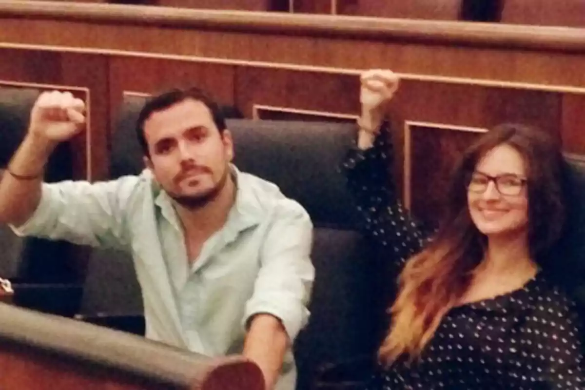 Dos personas sentadas en un recinto parlamentario levantan el puño en señal de saludo o protesta Dos personas sentadas en un recinto parlamentario levantan el puño en señal de saludo o protesta
