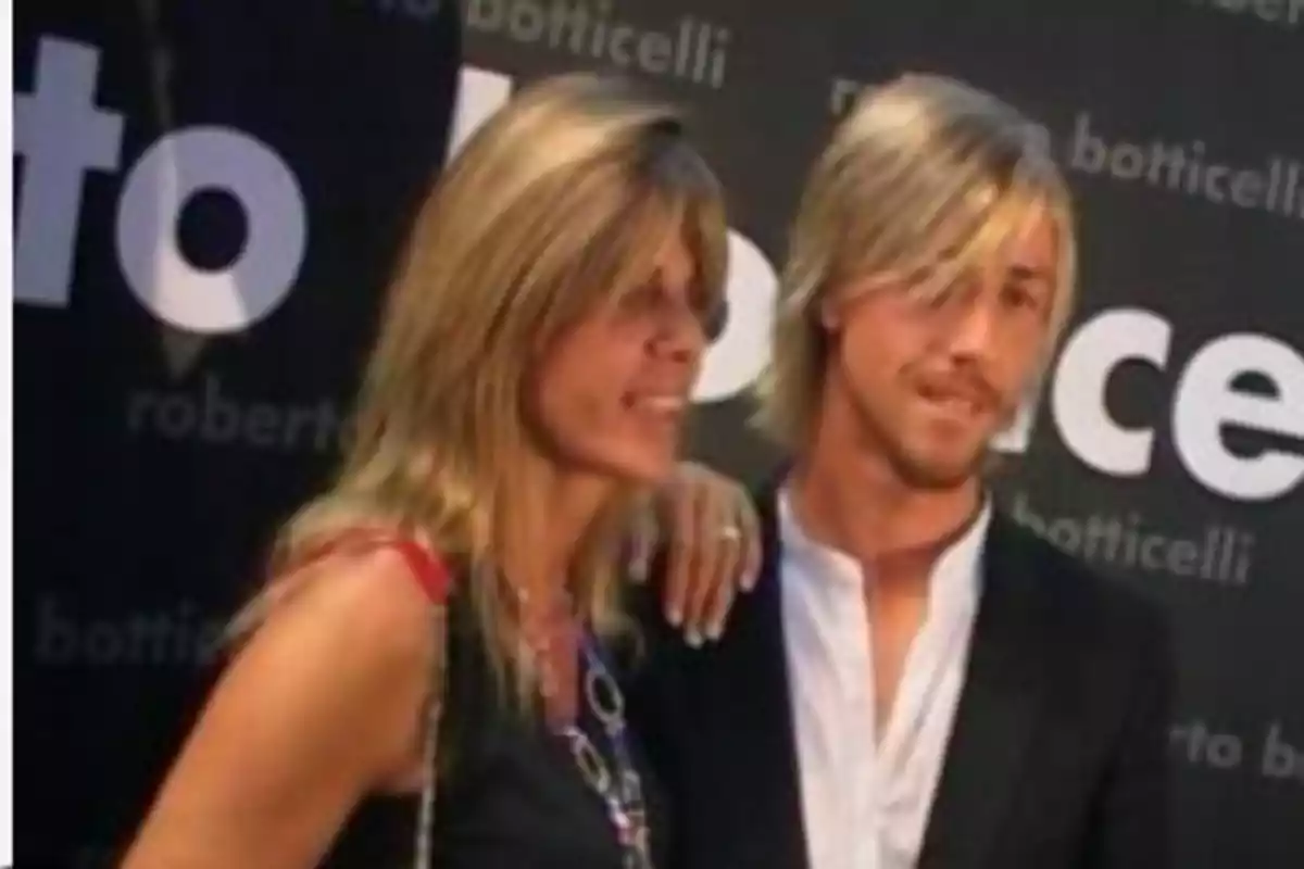 Dos personas posan juntas en un evento con fondo publicitario Dos personas posan juntas en un evento con fondo publicitario