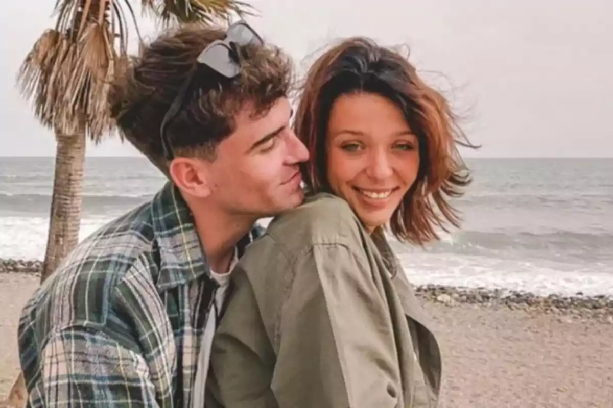 Pareja joven abrazándose y sonriendo en la playa con el mar y una palmera de fondo Pareja joven abrazándose y sonriendo en la playa con el mar y una palmera de fondo