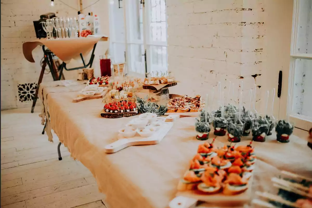 Mesa decorada con mantel rústico y variedad de aperitivos y bocadillos listos para un evento en un ambiente luminoso y elegante