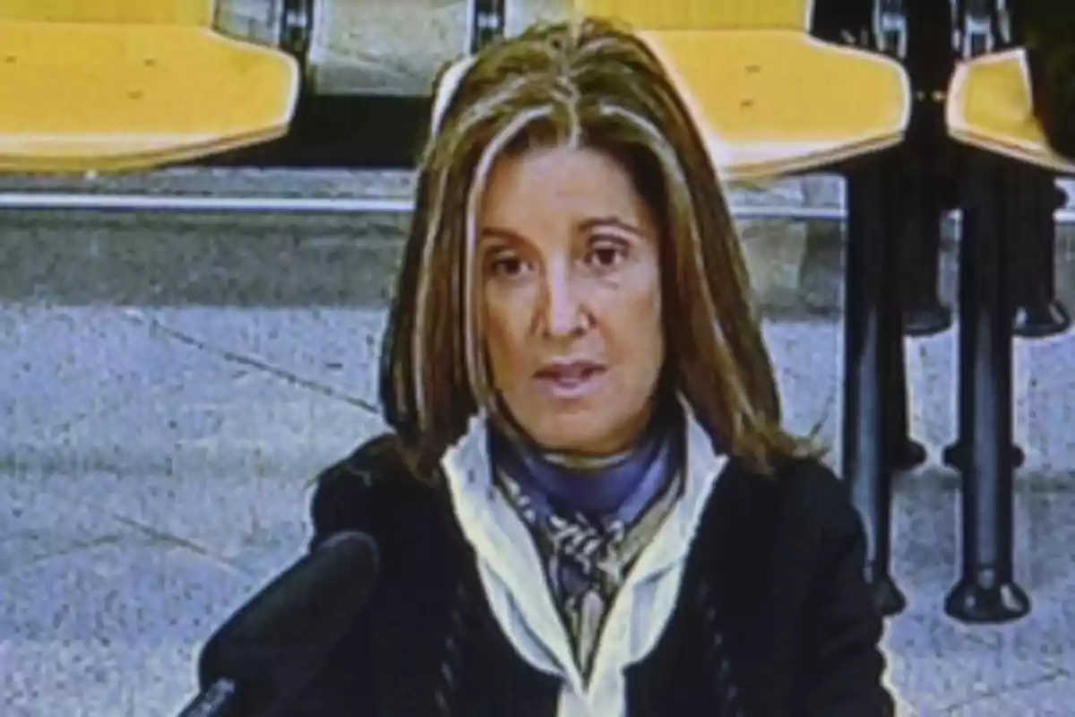 Mujer de cabello castaño con mechas rubias sentada frente a un micrófono en una sala con sillas amarillas Mujer de cabello castaño con mechas rubias sentada frente a un micrófono en una sala con sillas amarillas