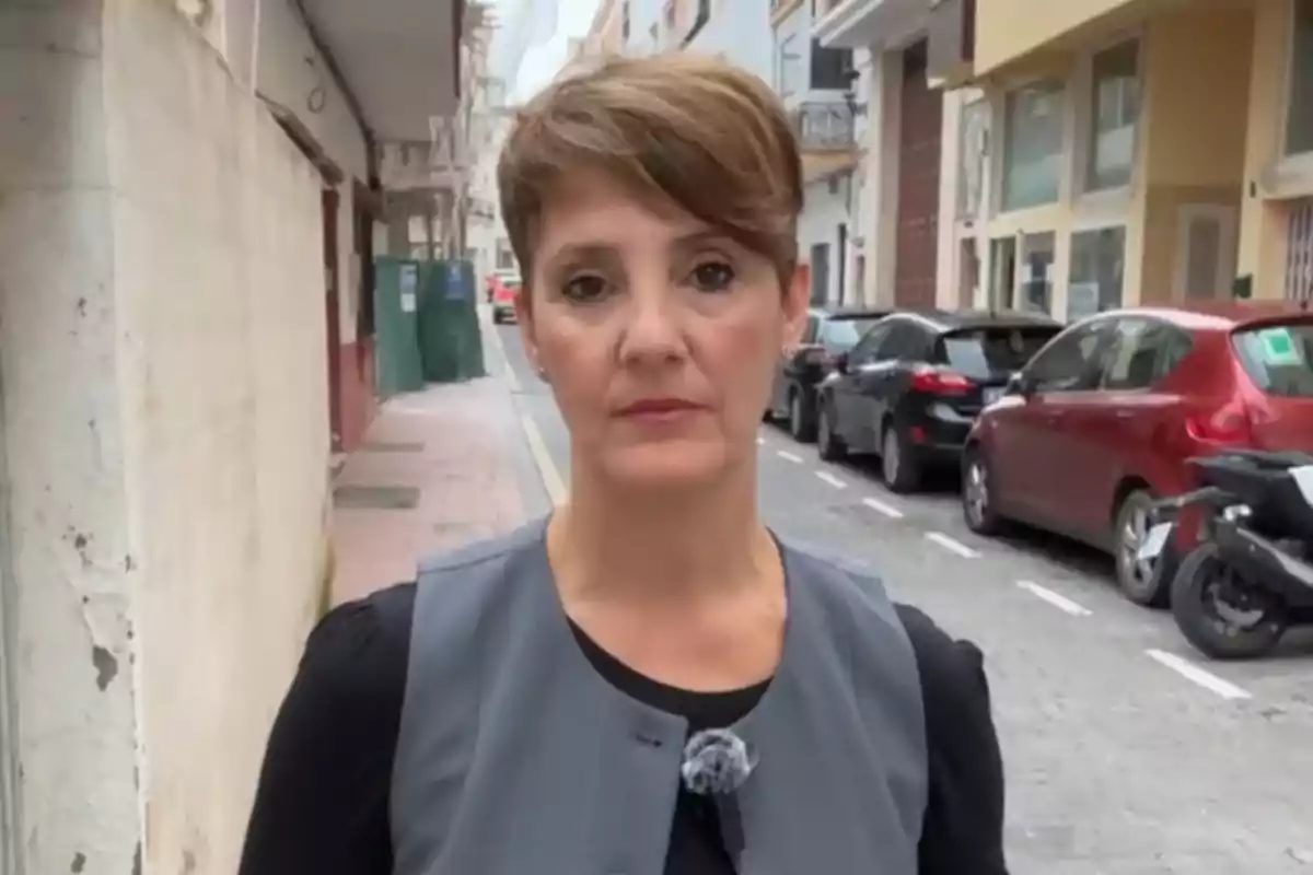 Mujer de cabello corto y castaño con expresión seria de pie en una calle urbana con autos estacionados al fondo Mujer de cabello corto y castaño con expresión seria de pie en una calle urbana con autos estacionados al fondo