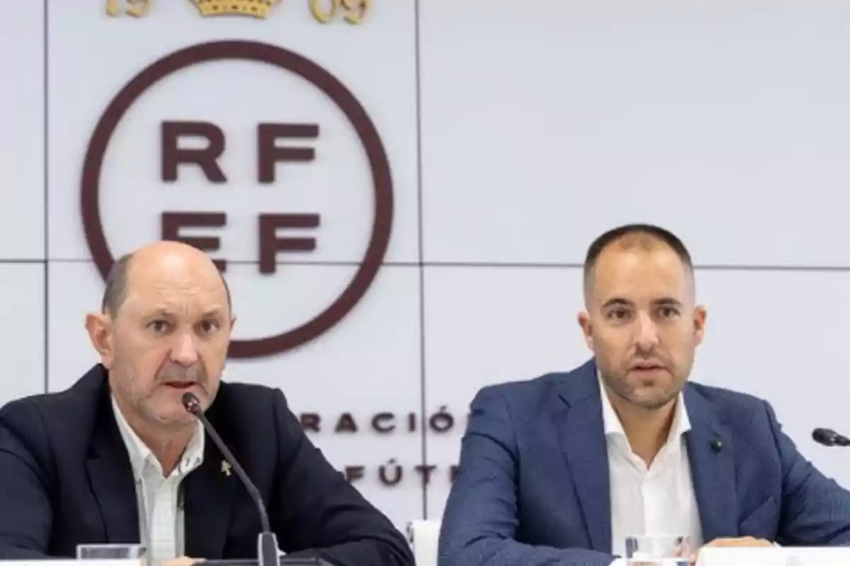 Dos hombres con traje sentados en una mesa durante una conferencia de prensa con el logo de la RFEF en el fondo