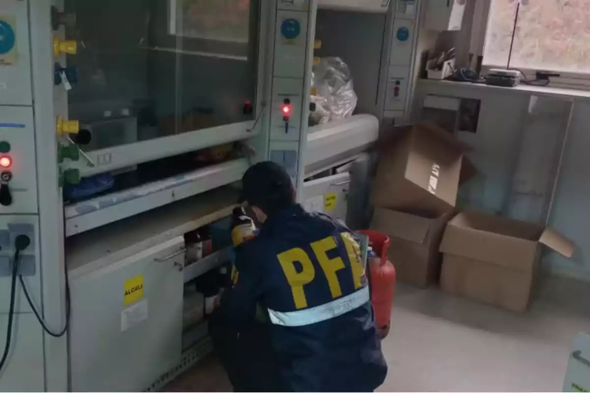 Agente de la PFA inspeccionando productos químicos en un laboratorio con cajas de cartón y un cilindro rojo en el suelo Agente de la PFA inspeccionando productos químicos en un laboratorio con cajas de cartón y un cilindro rojo en el suelo