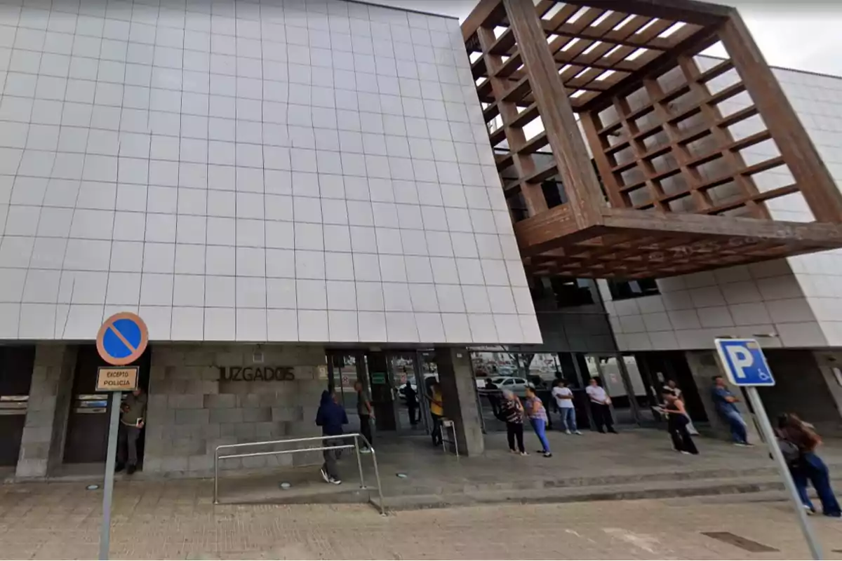 Fachada de un edificio moderno de juzgados con varias personas esperando en la entrada y señales de tráfico en la acera Fachada de un edificio moderno de juzgados con varias personas esperando en la entrada y señales de tráfico en la acera