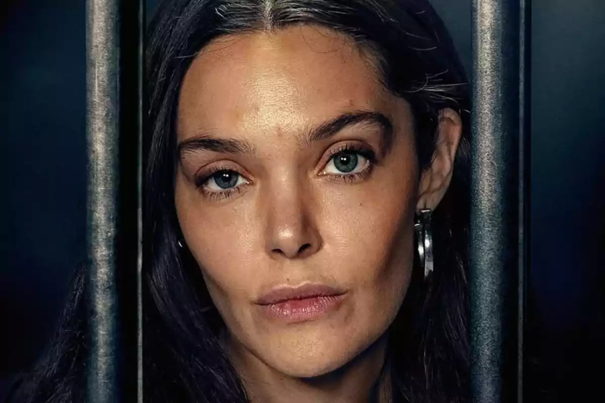 Mujer de cabello oscuro y ojos claros mirando al frente entre dos barrotes