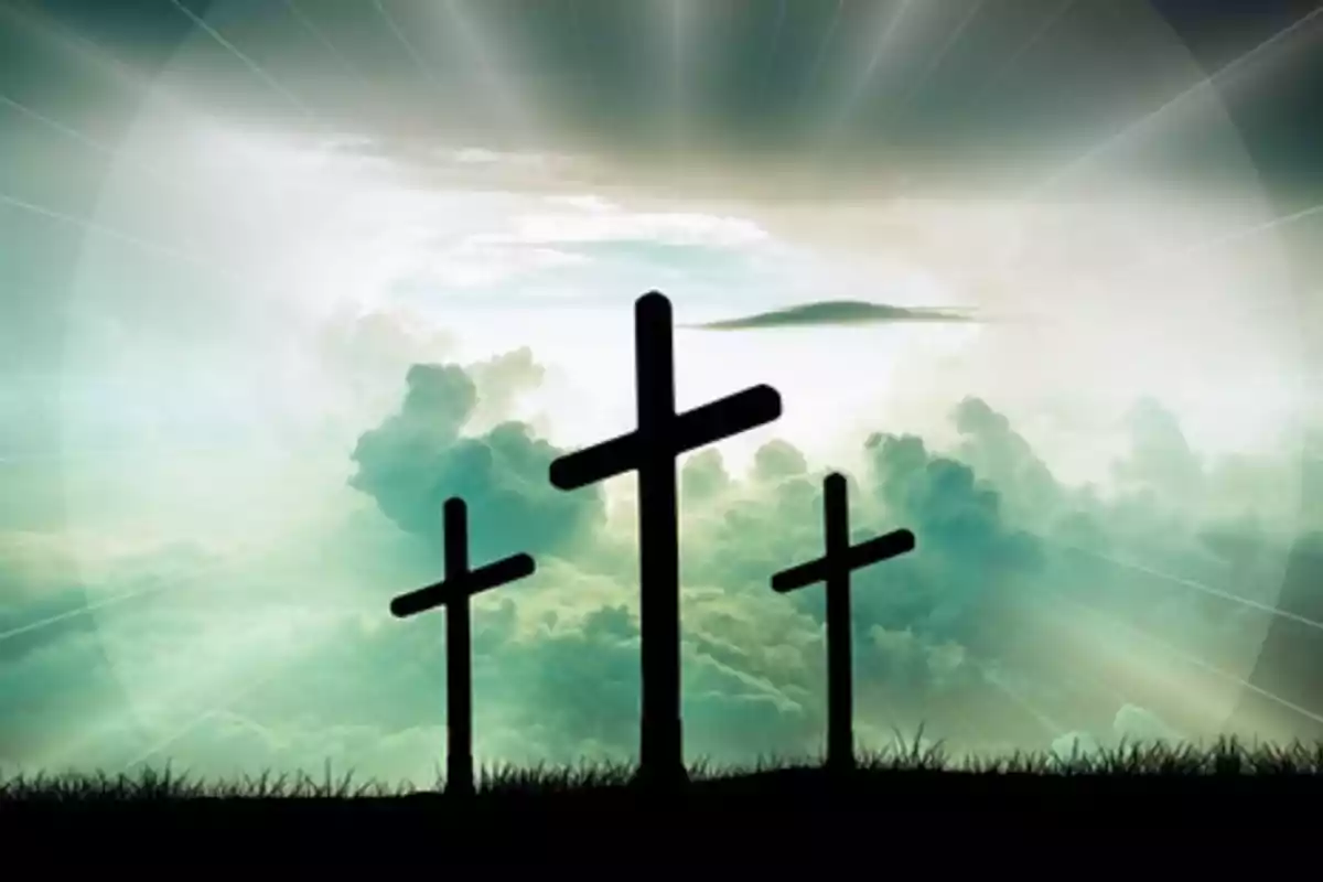 Tres cruces en una colina con un cielo nublado y rayos de luz al fondo