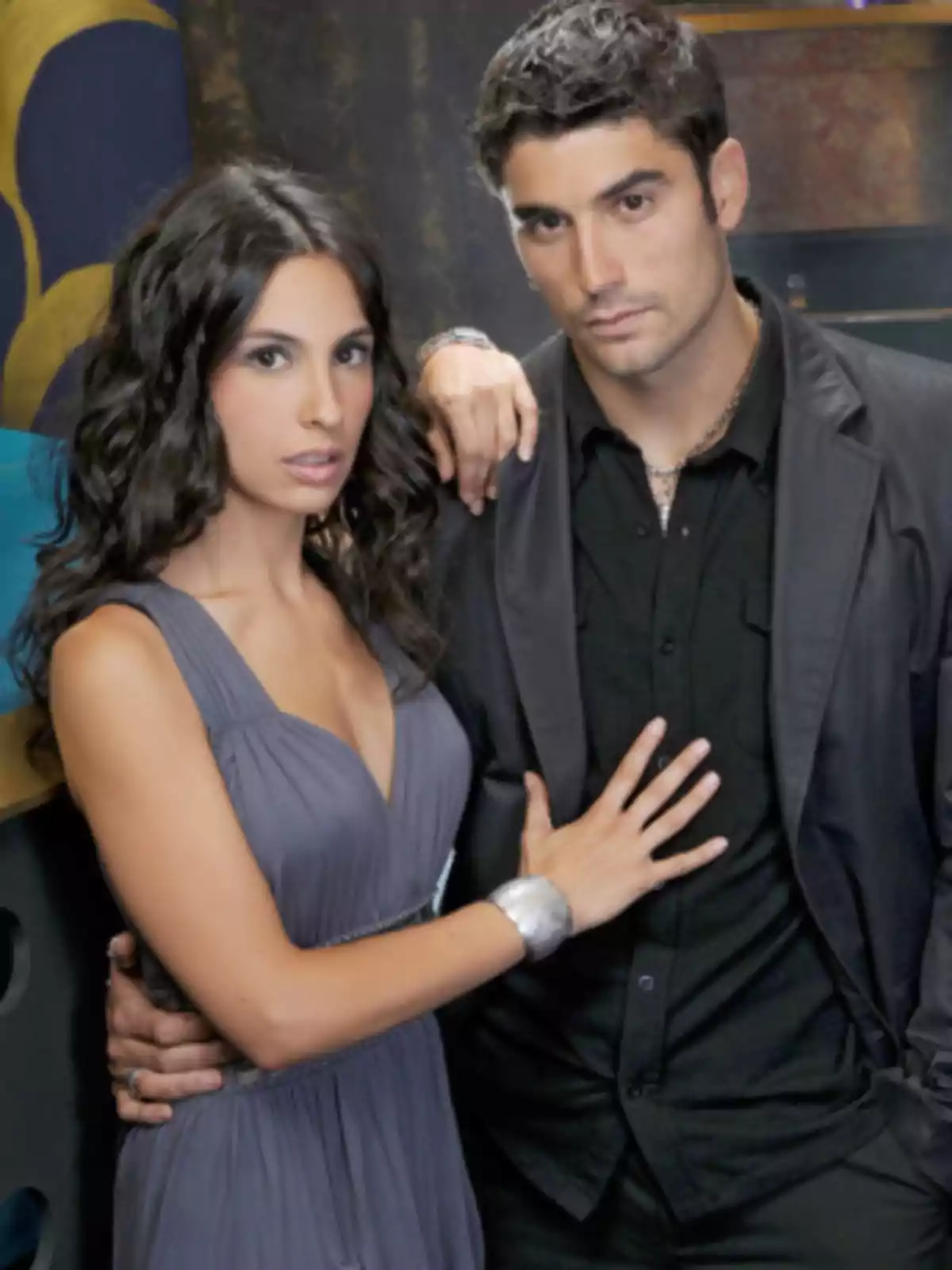 Pareja joven posando juntos con expresión seria y elegante, ella lleva un vestido gris y él viste de negro Pareja joven posando juntos con expresión seria y elegante, ella lleva un vestido gris y él viste de negro