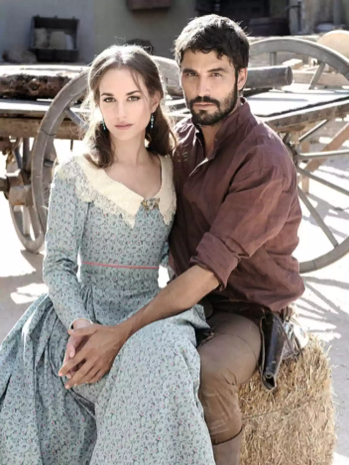 Una pareja vestida con ropa de época posa sentada frente a una carreta en un ambiente rural Una pareja vestida con ropa de época posa sentada frente a una carreta en un ambiente rural