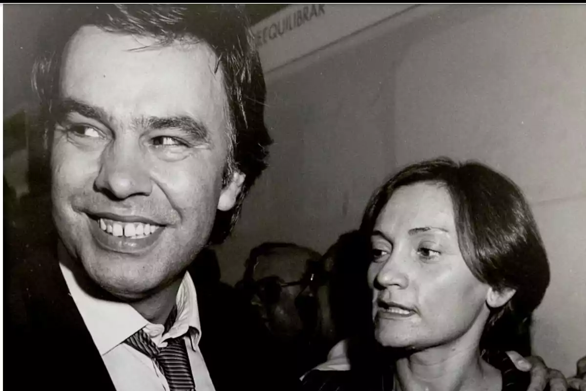 Un hombre sonriente con traje y corbata junto a una mujer de cabello corto en una fotografía en blanco y negro Un hombre sonriente con traje y corbata junto a una mujer de cabello corto en una fotografía en blanco y negro