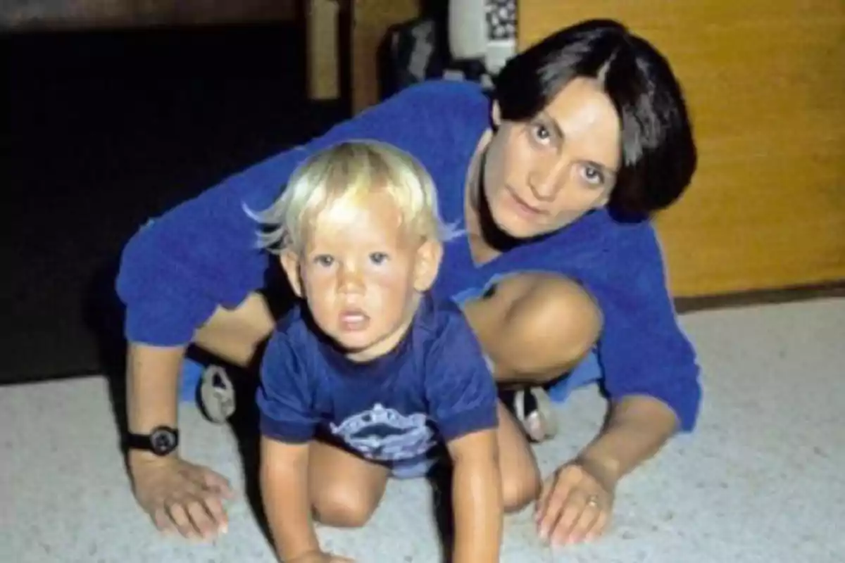 Una mujer y un niño pequeño rubio están en el suelo mirando hacia la cámara ambos vestidos con ropa azul Una mujer y un niño pequeño rubio están en el suelo mirando hacia la cámara ambos vestidos con ropa azul