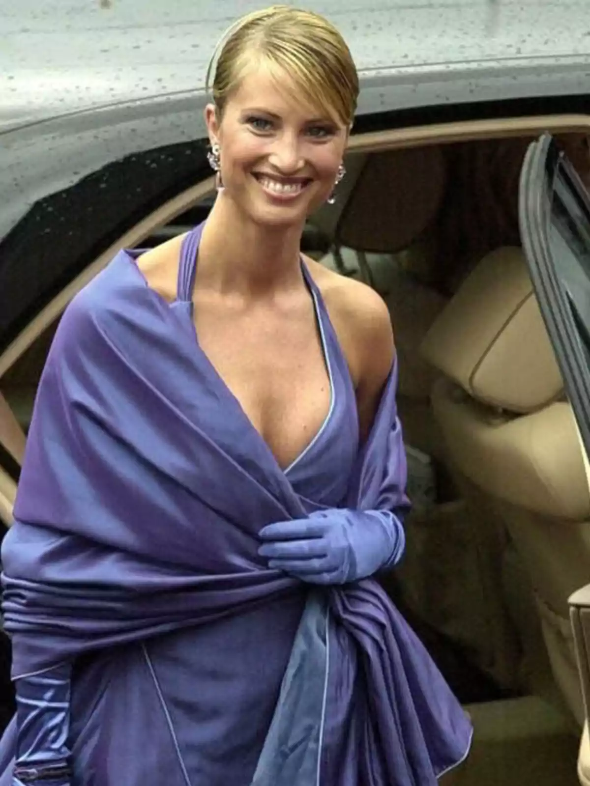 Mujer sonriente con vestido y guantes morados saliendo de un auto elegante Mujer sonriente con vestido y guantes morados saliendo de un auto elegante