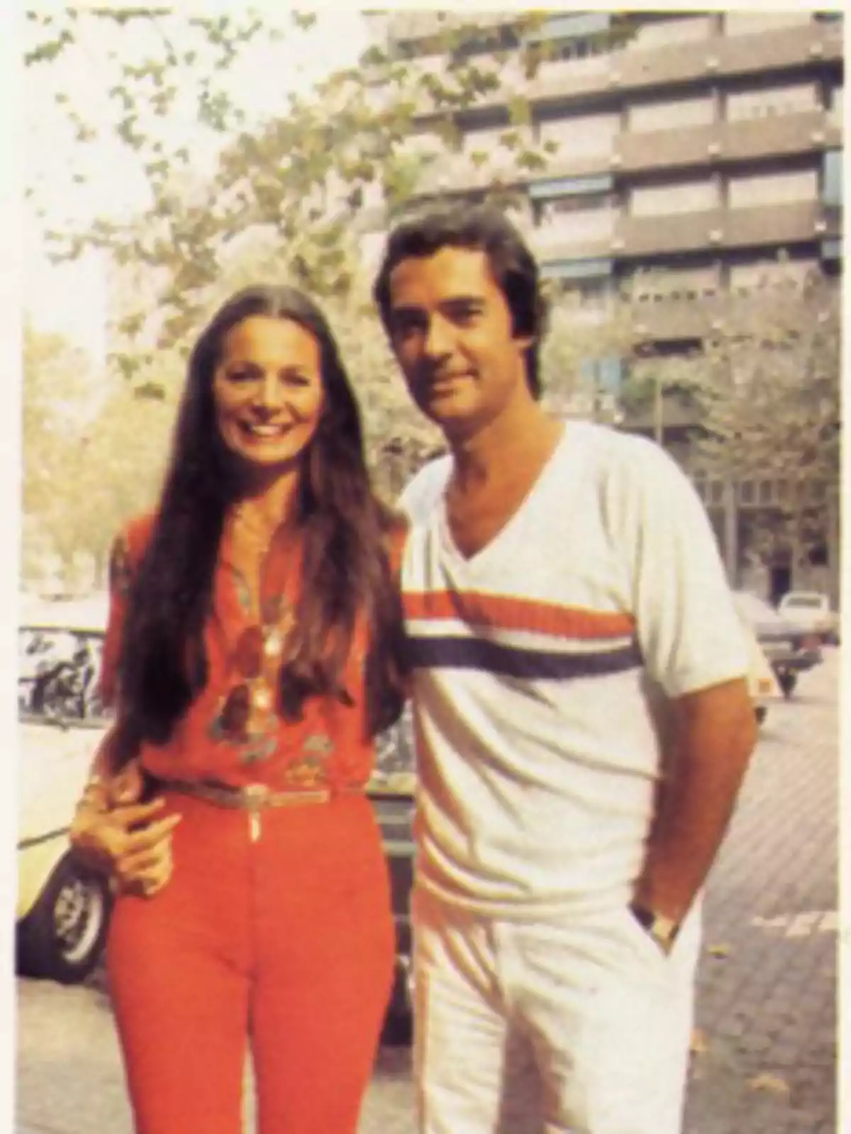 Una pareja sonriente posa en una calle arbolada con edificios al fondo Una pareja sonriente posa en una calle arbolada con edificios al fondo