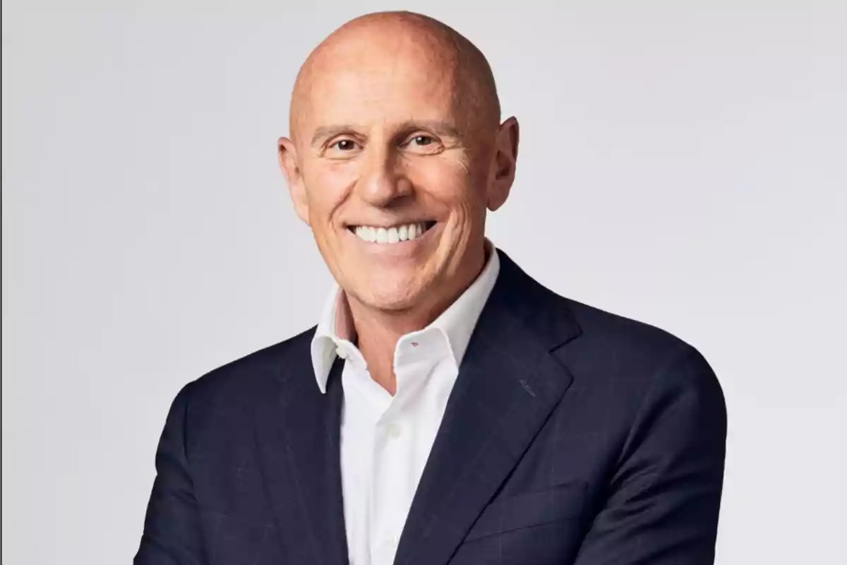 Hombre calvo de mediana edad sonriendo y vistiendo un traje azul marino con camisa blanca sobre fondo claro Hombre calvo de mediana edad sonriendo y vistiendo un traje azul marino con camisa blanca sobre fondo claro