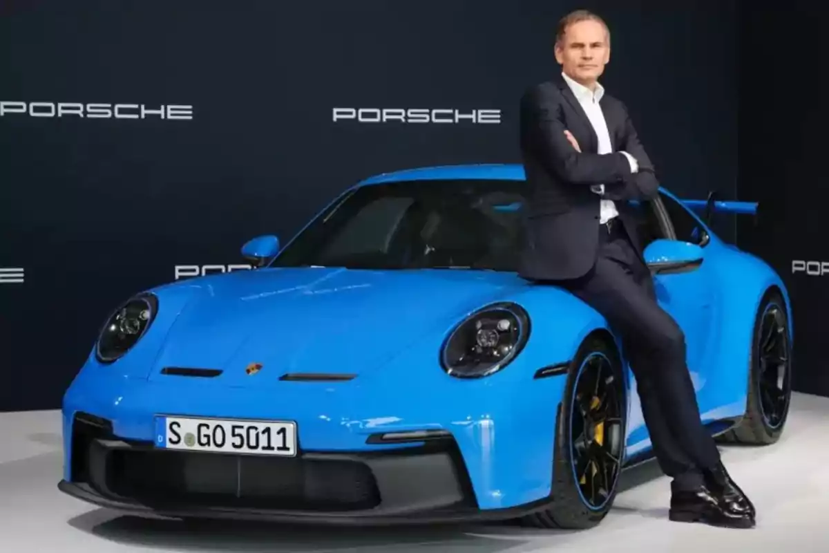 Hombre de traje apoyado en un auto deportivo azul de la marca Porsche en un evento de presentación Hombre de traje apoyado en un auto deportivo azul de la marca Porsche en un evento de presentación