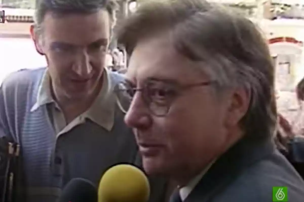 Dos hombres conversan mientras uno de ellos es entrevistado por varios micrófonos Dos hombres conversan mientras uno de ellos es entrevistado por varios micrófonos