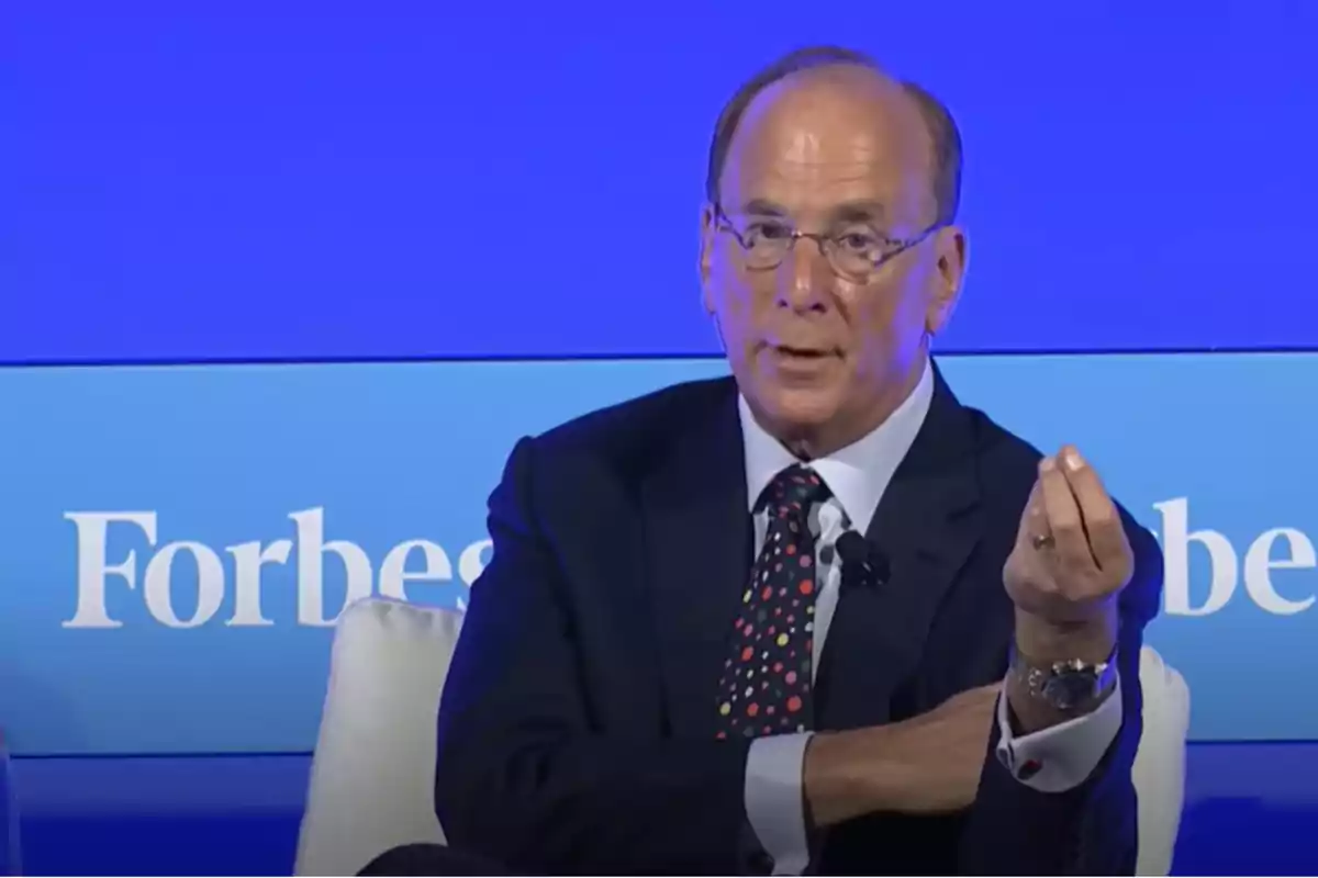Hombre de traje y corbata con puntos de colores hablando en un evento de Forbes con fondo azul