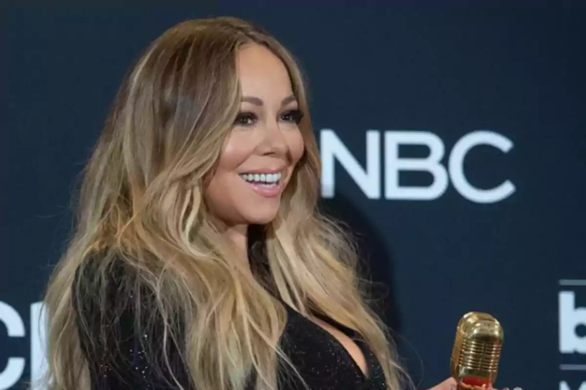 Mujer sonriente con micrófono dorado en un evento frente a un fondo con el logo de NBC