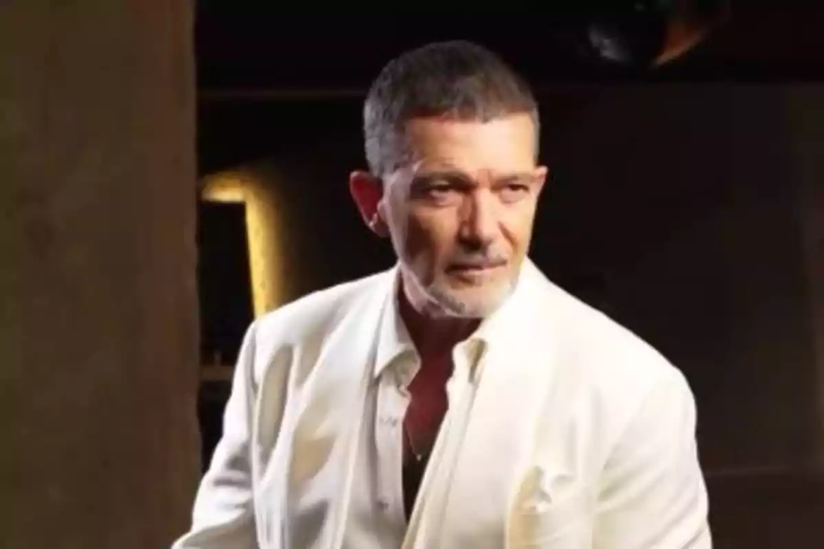 Hombre de cabello corto y barba canosa vistiendo un saco blanco en un ambiente interior con luz tenue