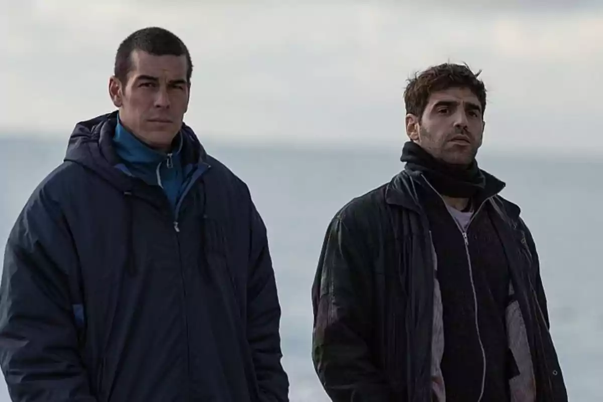 Dos hombres con ropa de abrigo están de pie junto al mar en un día nublado Dos hombres con ropa de abrigo están de pie junto al mar en un día nublado