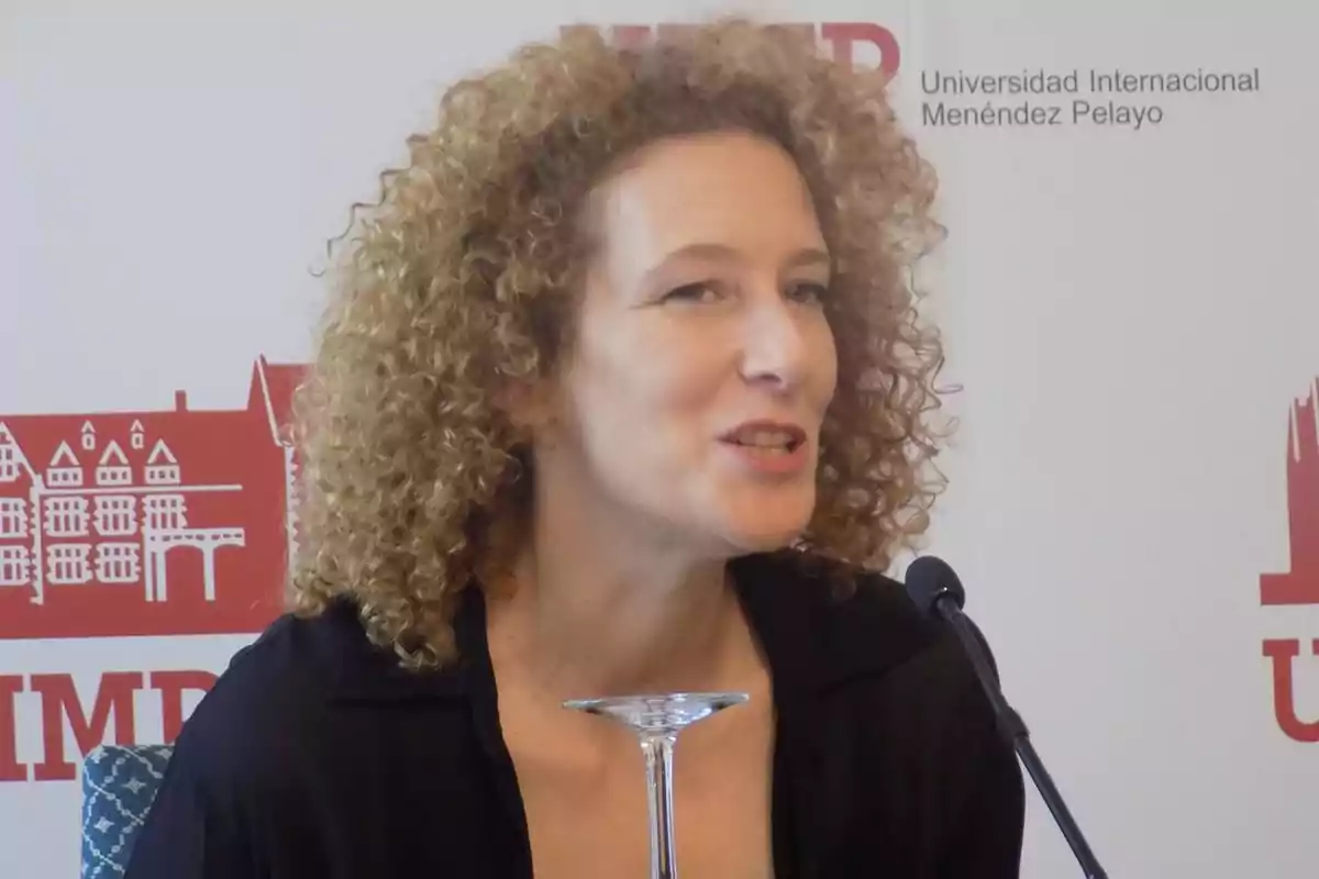 Mujer de cabello rizado hablando frente a un micrófono en un evento de la Universidad Internacional Menéndez Pelayo