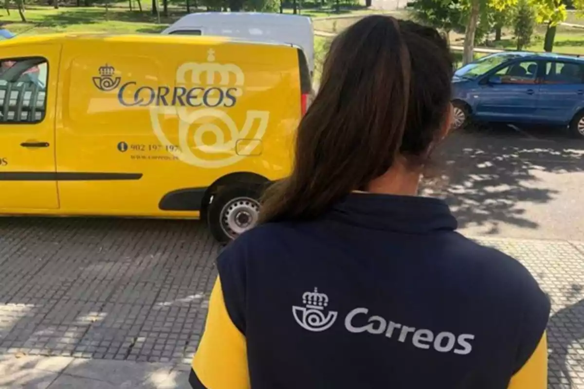 Trabajadora de Correos de espaldas frente a una furgoneta amarilla de la empresa en la calle