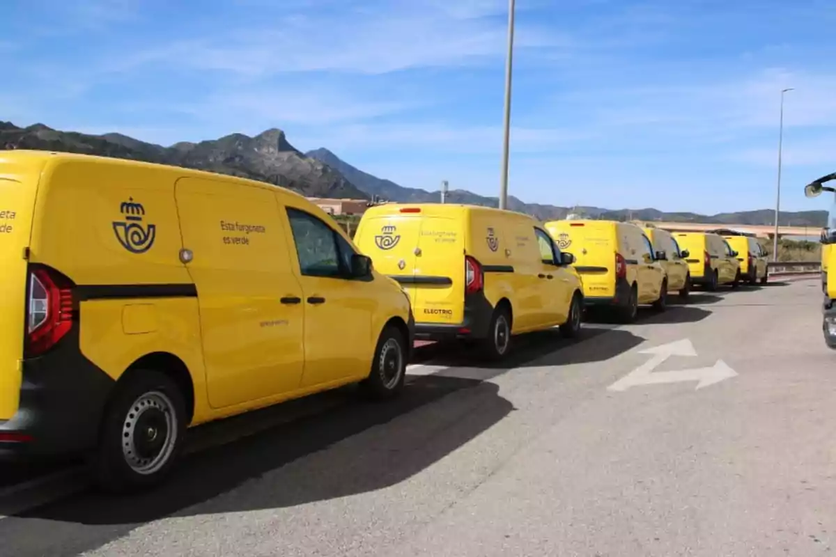 Varios vehículos de reparto amarillos alineados en una carretera con montañas al fondo Varios vehículos de reparto amarillos alineados en una carretera con montañas al fondo